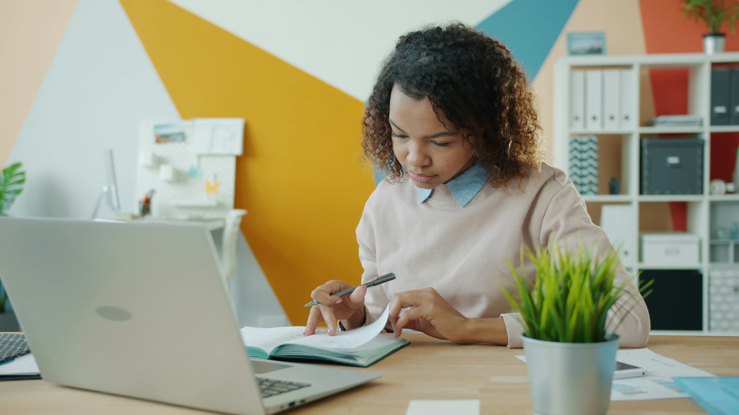 A researcher writing in a notebook beside a laptop
